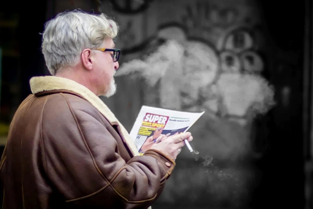 Older man reading a leaflet while smoke drifts from his mouth